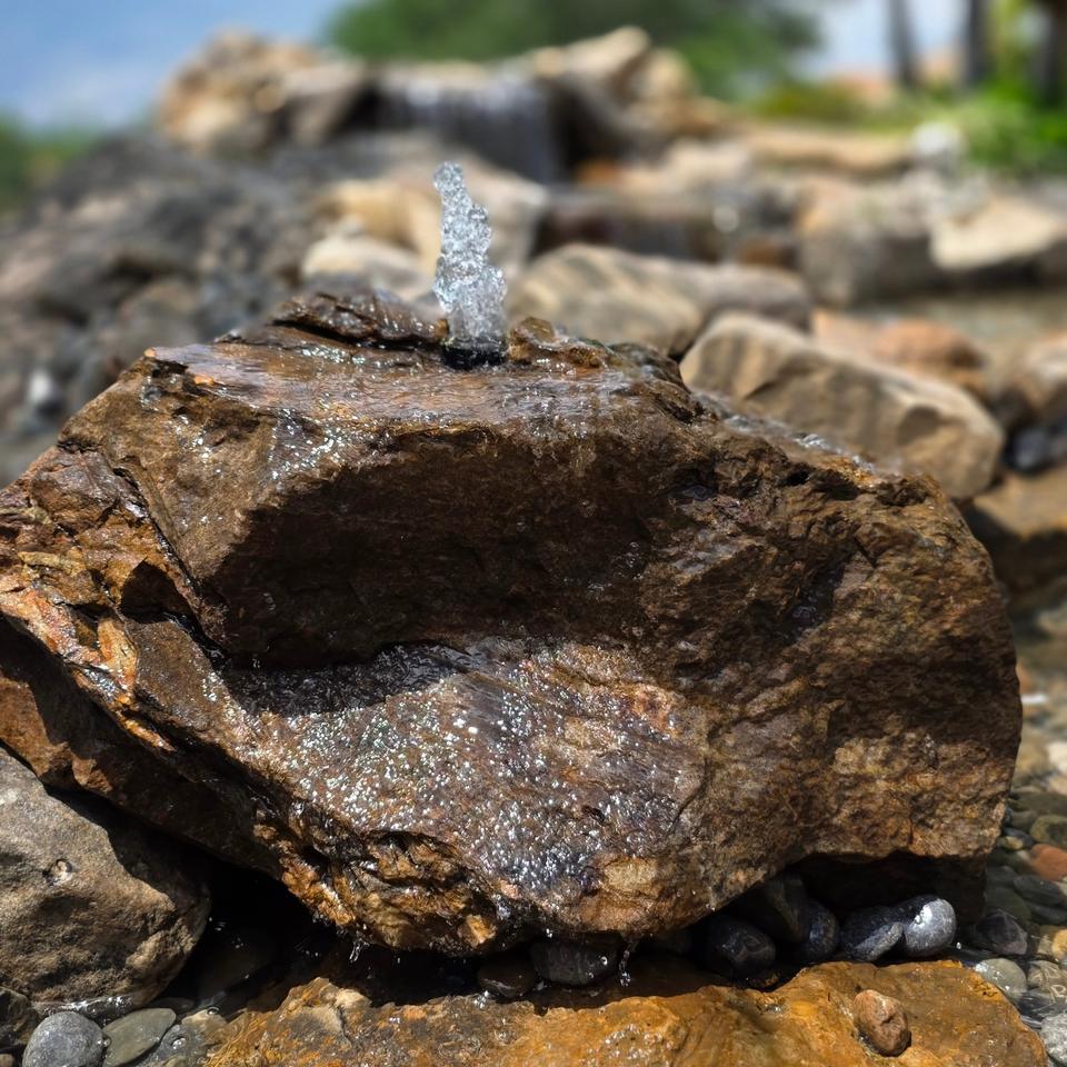 Large brown boulder with water bubbling over its top, set in stacked stone and river rock