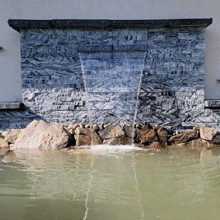 Sheer water spillway pouring from a grey stacked-slate wall