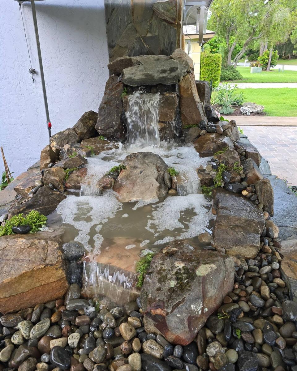 Pondless waterfall cascading down fieldstone boulders in a stacked-stone planter in front of a house