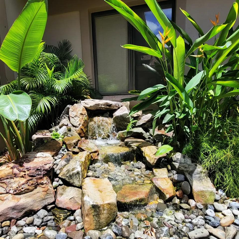 Small waterfall stepping down tan boulders beside a house