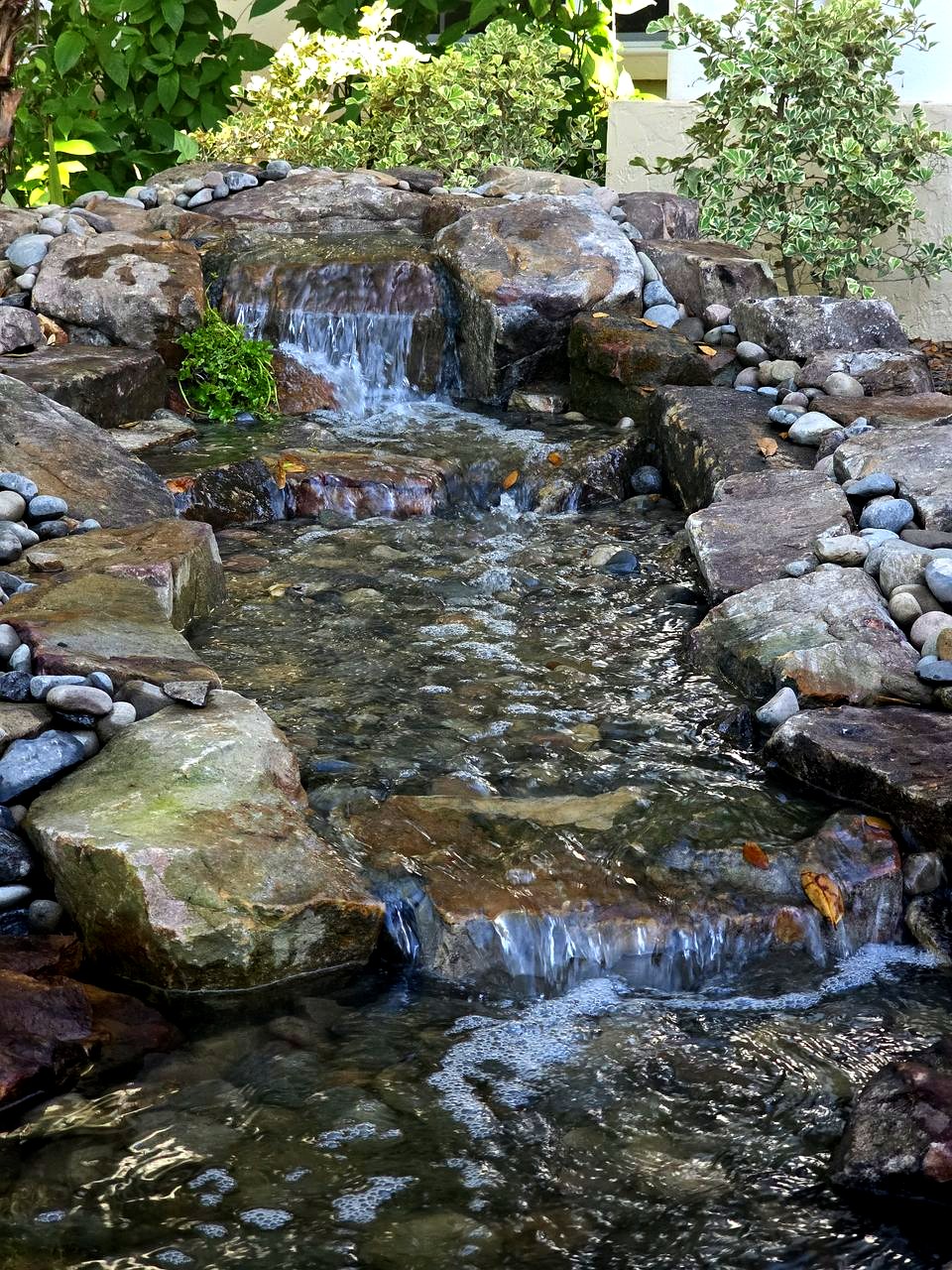 Close-up of a pondless waterfall: water spilling down tiers of flat stone ledges and flowing over river rock, with no open pond