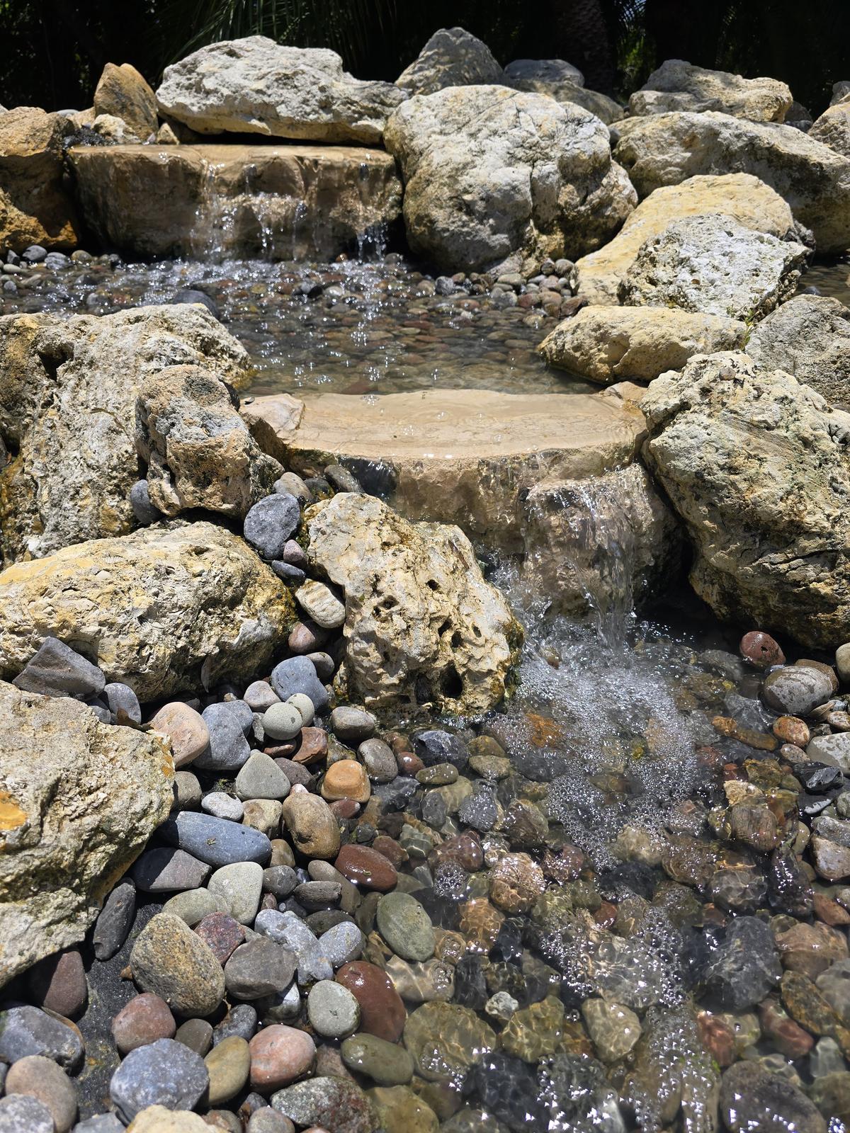 Clear water spilling over flat tan stone ledges into a rock-lined stream bed
