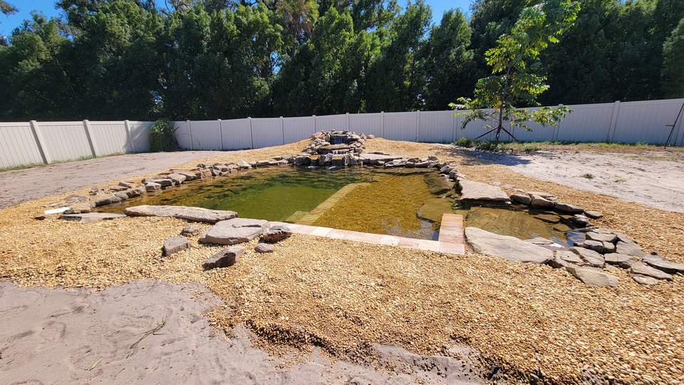 Recreational swim pond with gravel beach entry and rock waterfall beyond