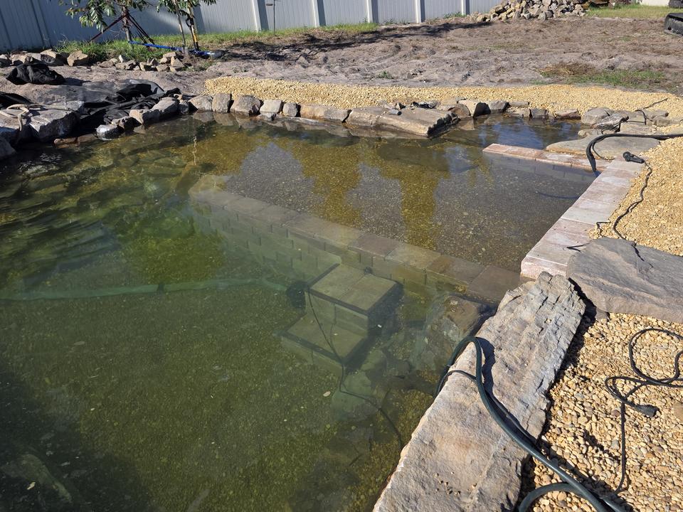 Recreational swim pond during late build — submerged entry steps and rock edge