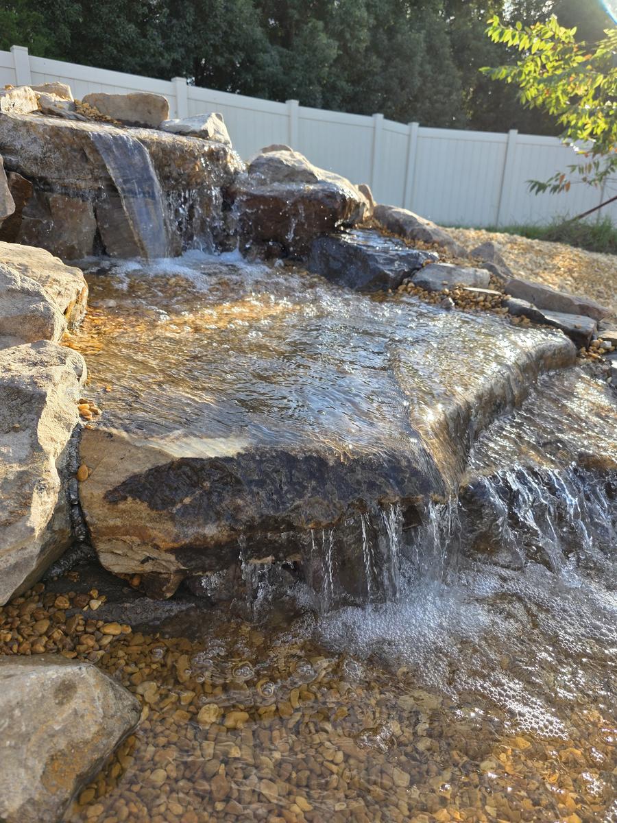 Multi-tier rock waterfall cascading into clear swim-pond water