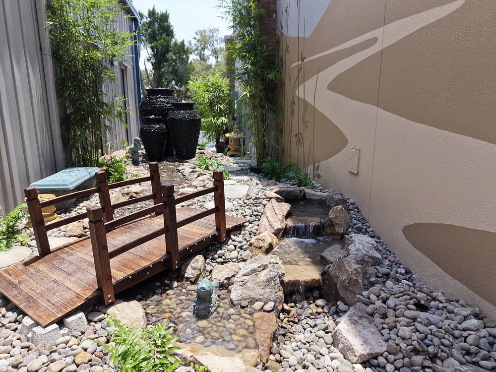 Zen garden alley with bubbling black urns, a rock stream and a wooden bridge